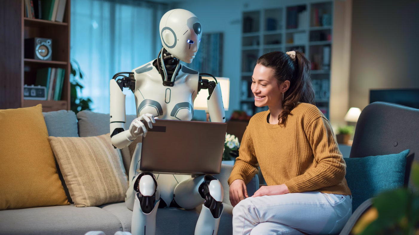A girl working on a laptop with a robot